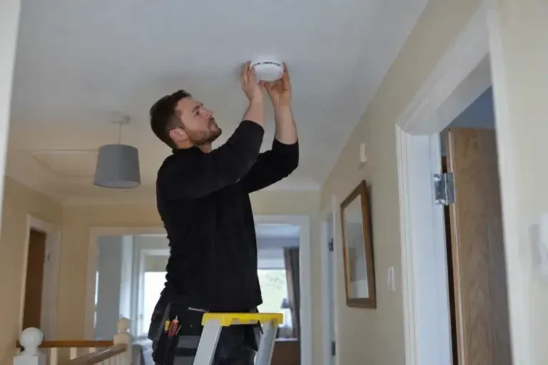 Technician fitting a ceiling-mounted smoke alarm in a hallway