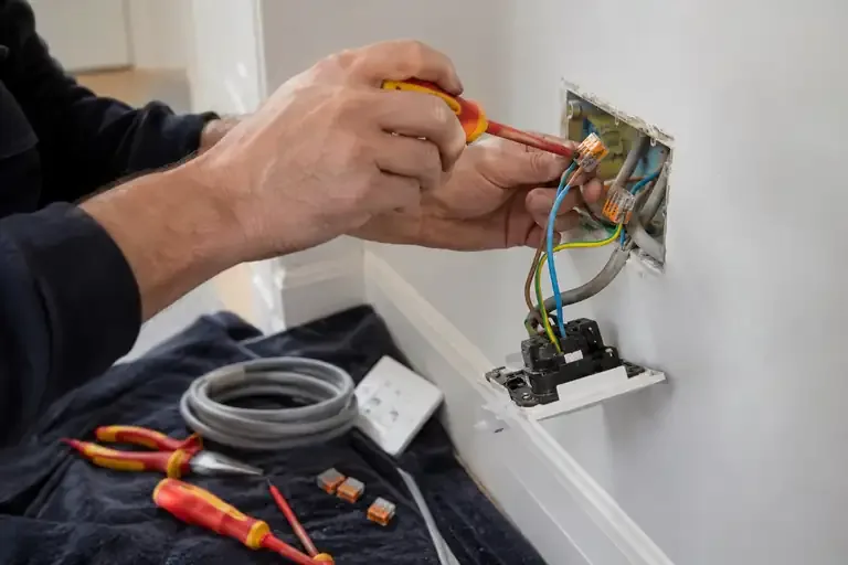 Electrician repairing isolated socket wiring with insulated tools and enclosed connectors.